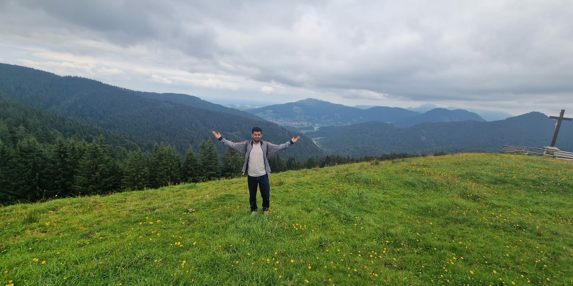Hier posiert ein junger Mann vor einer bergigen Landschaft und hebt die Arme hoch.
